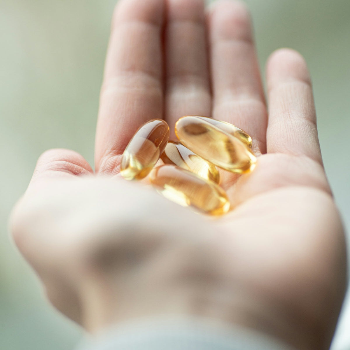 Golden supplement softgels held in an open palm in natural light