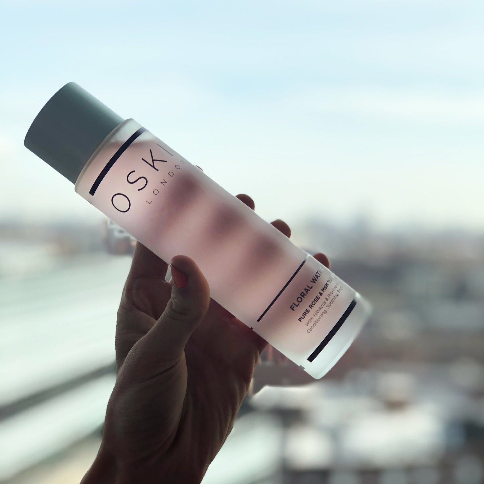 Hand holding a bottle of Oskia Floral Water Toner