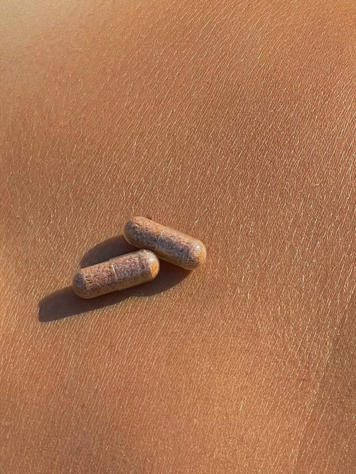 Atelier Nubio A Summer Tan, S'il Vous Plait two capsules resting on sun-kissed skin