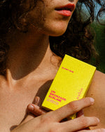 Atelier Nubio A Summer Tan, S'il Vous Plait model holding the yellow box in the sunshine