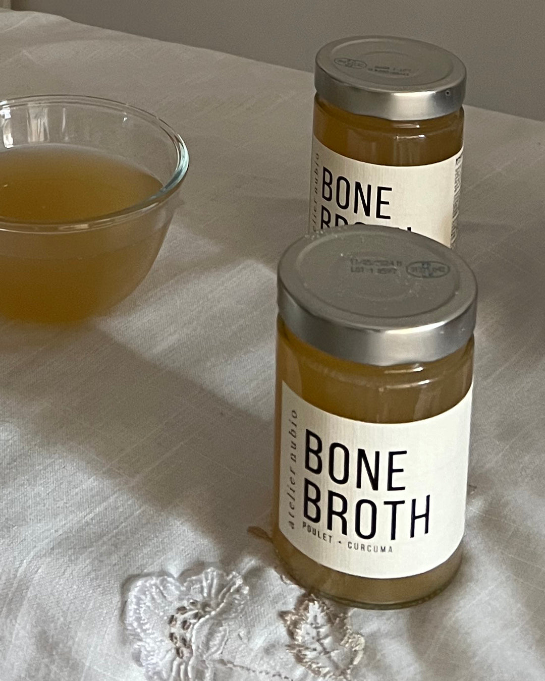 Atelier Nubio Bone Broth Chicken & Turmeric jars beside a bowl of warmed broth