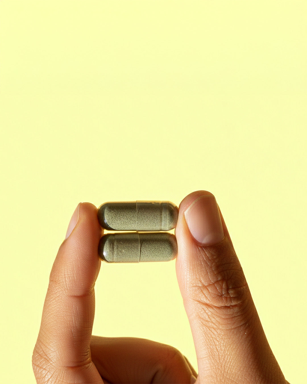 Atelier Nubio Long Luscious Hair, S'il Vous Plait two green plant capsules held between finger and thumb