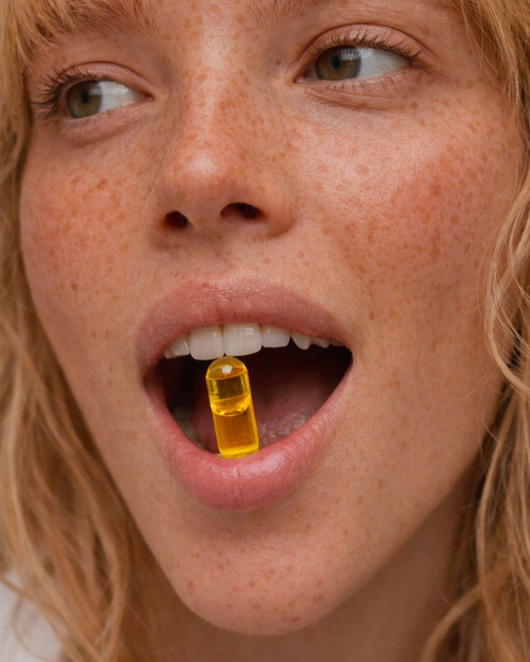 Atelier Nubio Plump Up My Skin, S'il Vous Plait model holding a golden capsule between her teeth