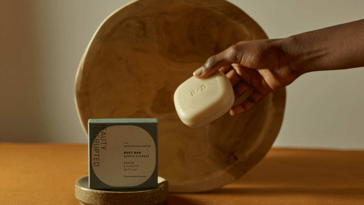 Hand holding the Beauty Disrupted Body Bar in front of a wooden platter with the Amazonian Amour box