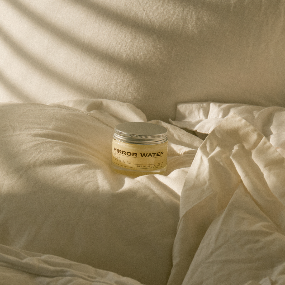 MIRROR WATER RUB Solid Balm jar on cream bed linen in sunlight