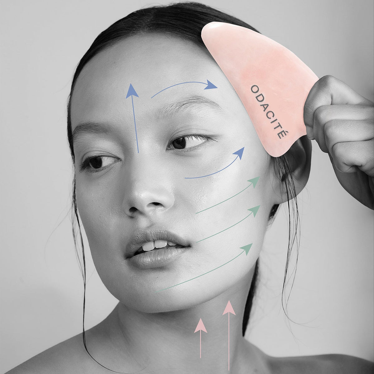 Odacité Crystal Contour Gua Sha Rose Quartz in use on the face with massage-direction arrows