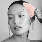 Odacité Crystal Contour Gua Sha Rose Quartz in use on the face with massage-direction arrows