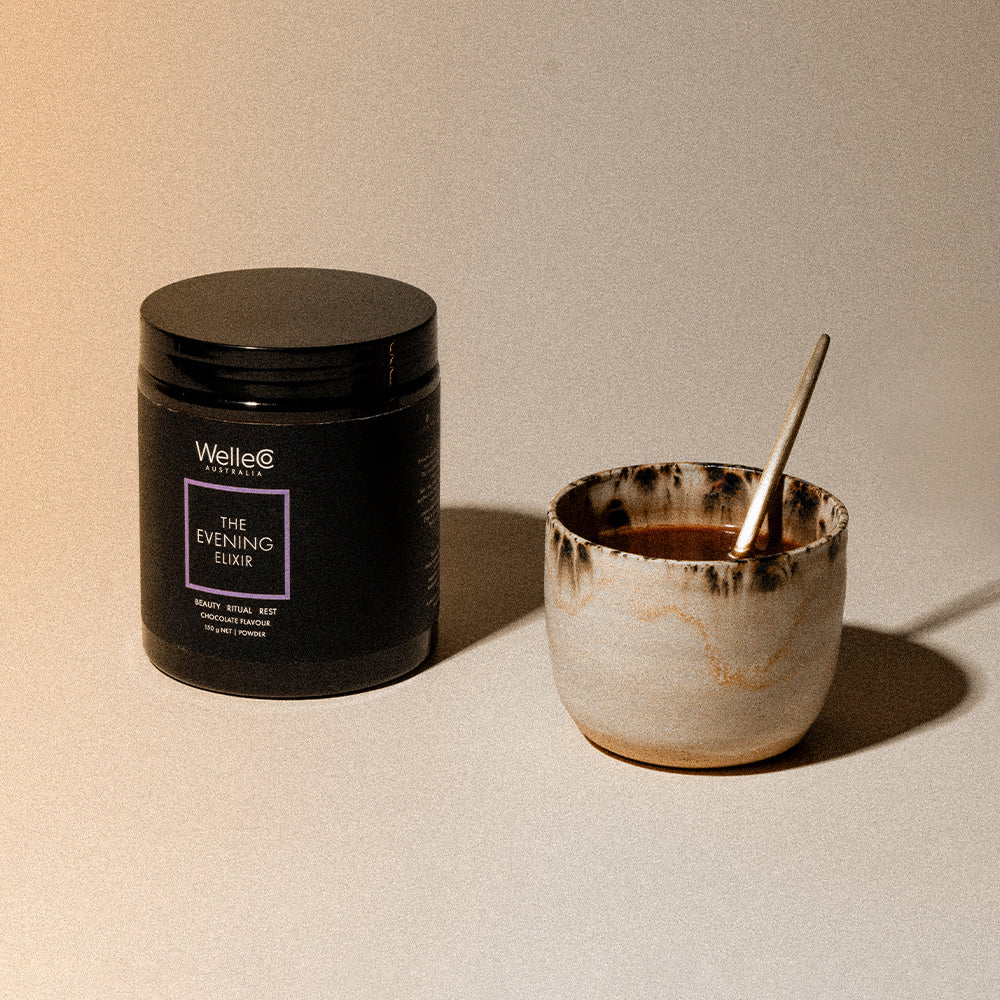WelleCo The Evening Elixir jar beside a ceramic cup of hot chocolate with a gold spoon